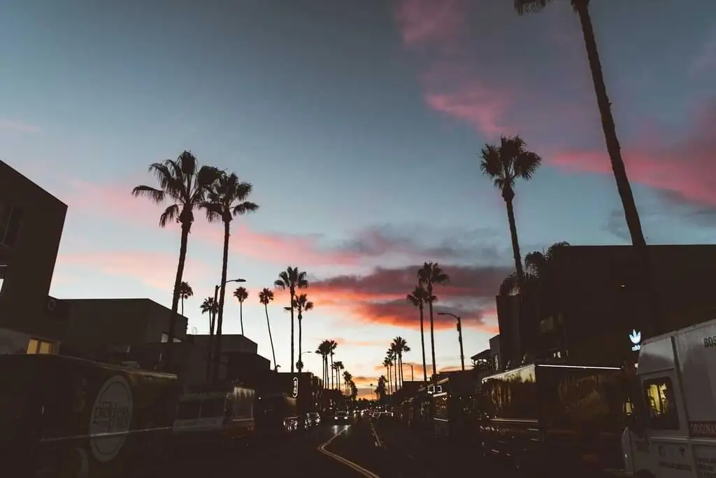 Calle de Hollywood al anochecer con siluetas de palmeras contra un cielo con tonos rosados y azules."