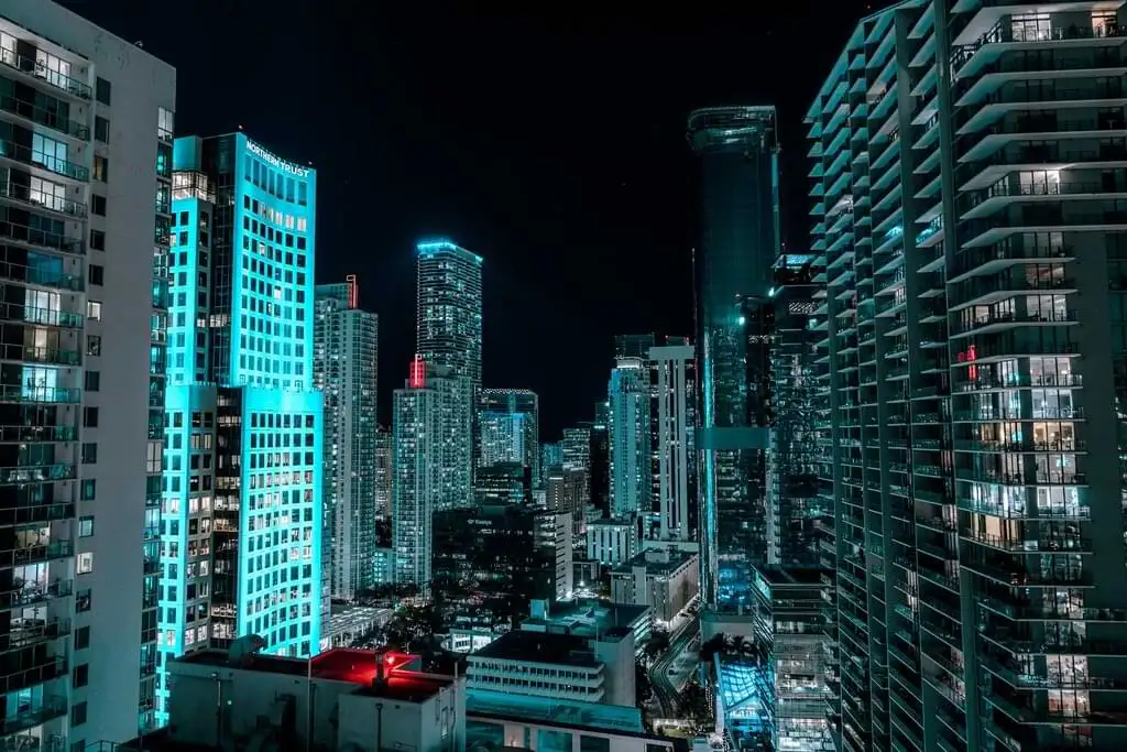 Vista nocturna de los rascacielos de Miami iluminados en tonos de azul neón, destacando la vibrante vida urbana y arquitectura moderna