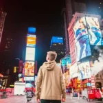 Hombre de espaldas contemplando las vibrantes luces y pantallas publicitarias en Times Square, Nueva York, de noche