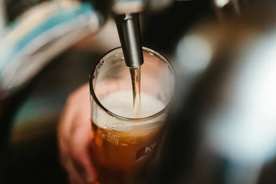 Cerveza ámbar vertida desde un grifo en una pinta con espuma cremosa, enfoque selectivo en el grifo