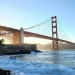 Vista del Golden Gate Bridge en San Francisco durante el atardecer, con olas chocando contra la orilla y un cielo despejado