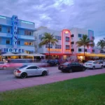 Vista crepuscular de Ocean Drive con hoteles Art Decó iluminados en neón, coches en movimiento y palmeras en Miami Beach, evocando una vibrante atmósfera nocturna